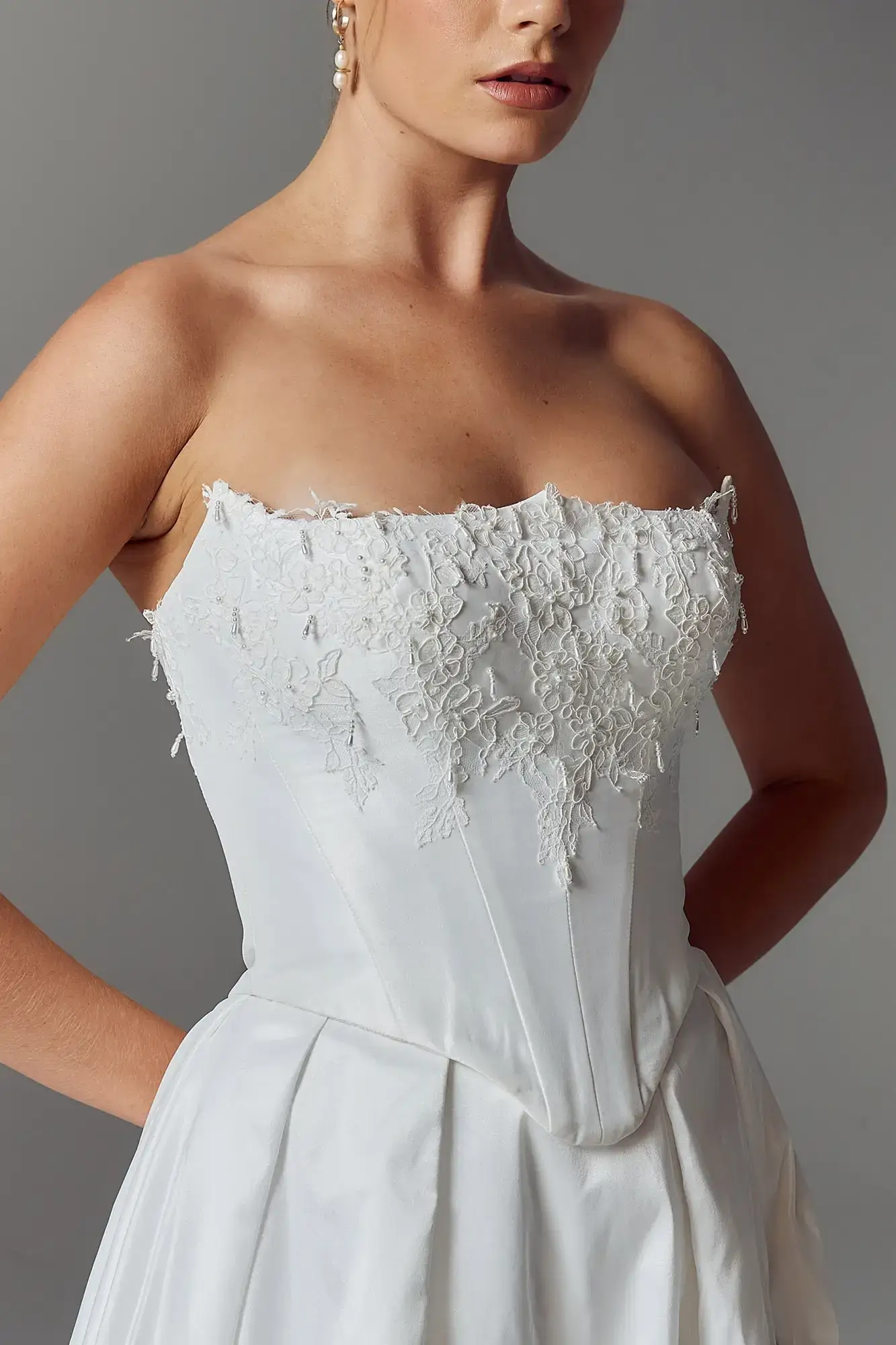 A close-up of a woman wearing a strapless wedding dress with intricate floral lace detailing on the bodice.