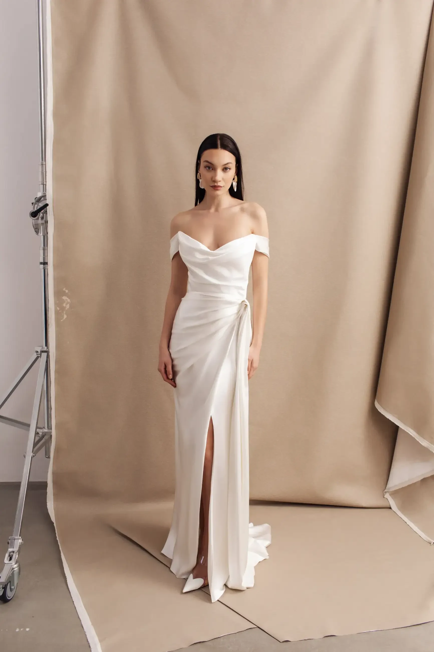 model is wearing a sleek off the shoulder ruched fit and flare bridal gown