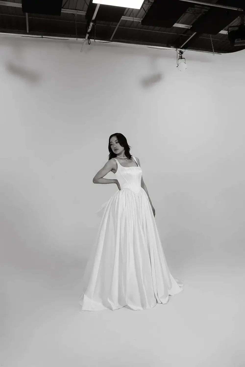 A model poses in a studio wearing a elegant white gown against a plain background.